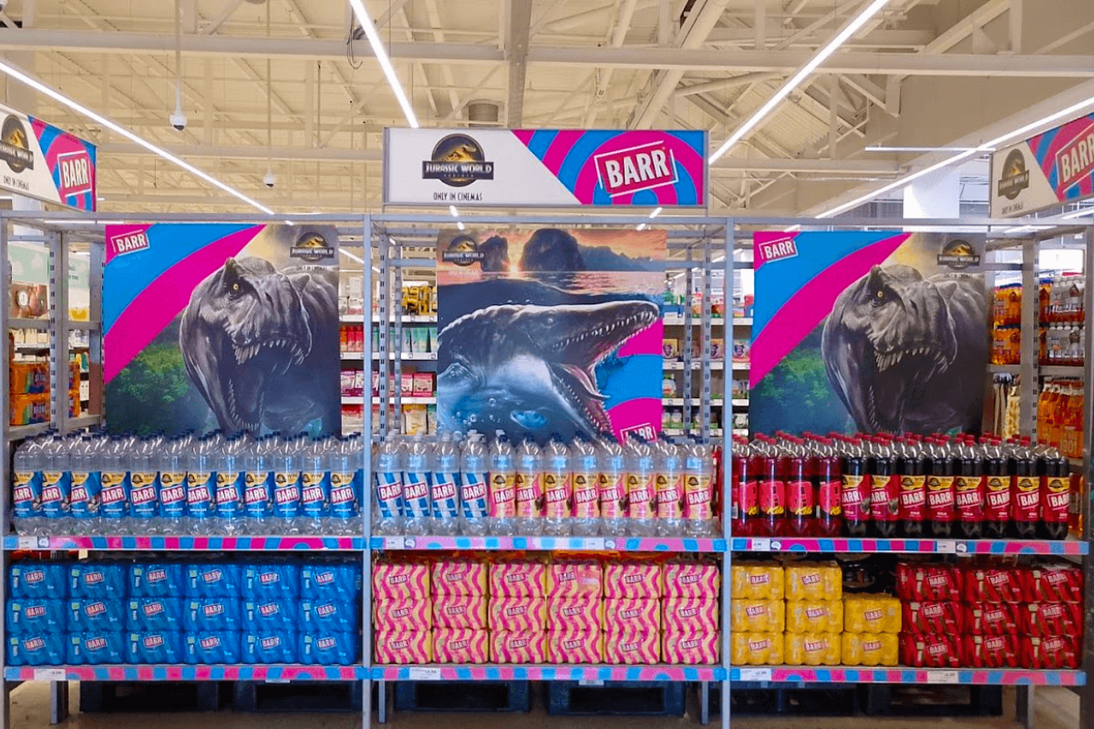 a stand in a shop showing the Barr Jurassic World instore promotion with bottles of Barr bottles and Jurassic world photos.